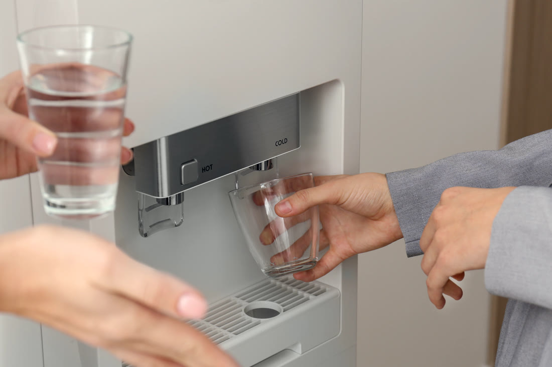Dos personas de una oficina sirviéndose agua fría del dispenser.